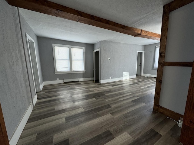 empty room with beam ceiling, a textured ceiling, and dark wood-type flooring