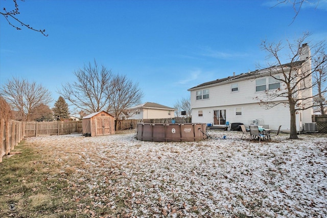 snow covered house with a fenced in pool and a storage unit