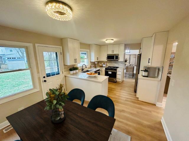 kitchen with kitchen peninsula, appliances with stainless steel finishes, sink, light hardwood / wood-style floors, and white cabinetry