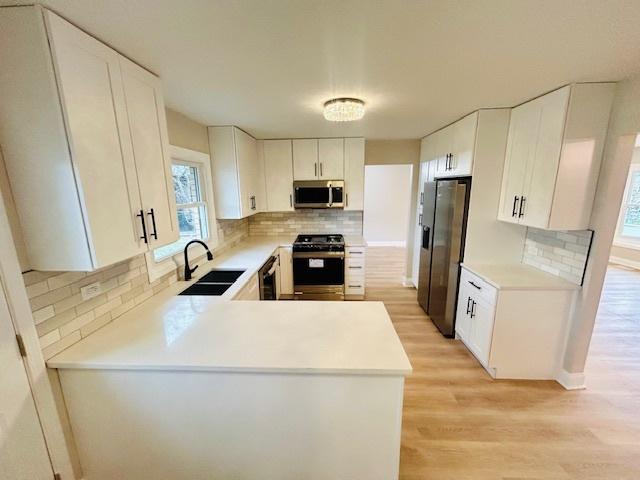 kitchen featuring tasteful backsplash, sink, black appliances, light hardwood / wood-style flooring, and white cabinetry