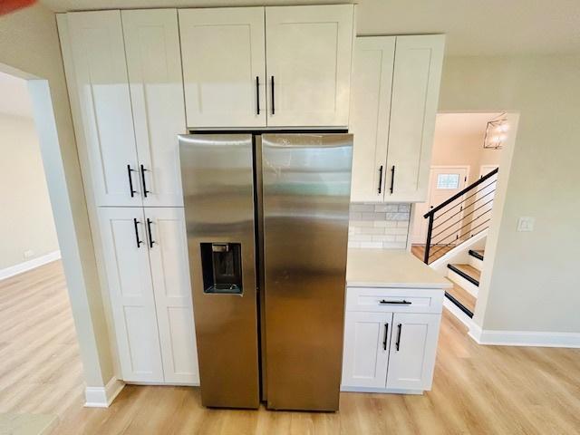 kitchen with white cabinets, stainless steel fridge, backsplash, and light hardwood / wood-style floors