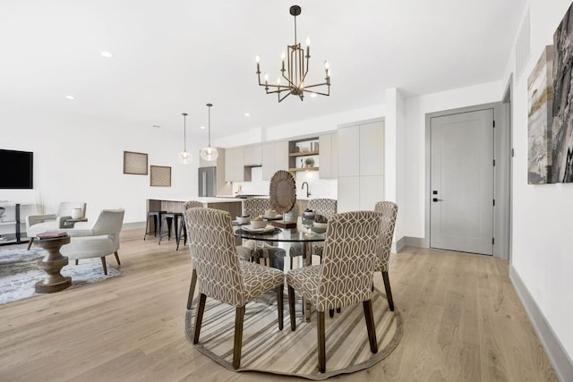 dining room with sink, light wood-type flooring, and an inviting chandelier