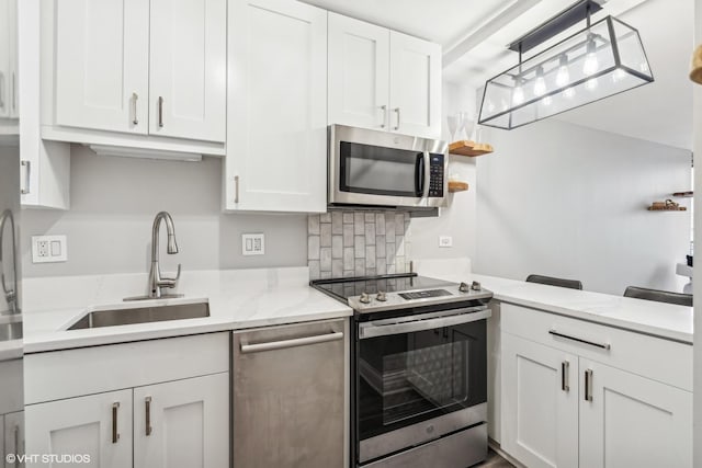 kitchen with white cabinetry, sink, hanging light fixtures, light stone counters, and appliances with stainless steel finishes