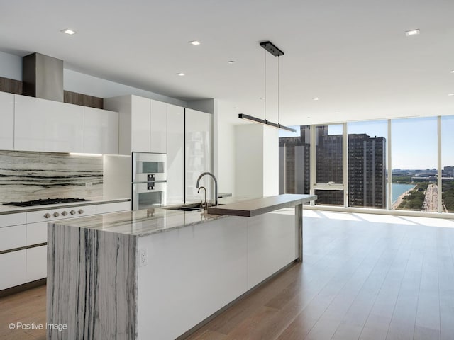 kitchen with white cabinets, an island with sink, a water view, and hanging light fixtures