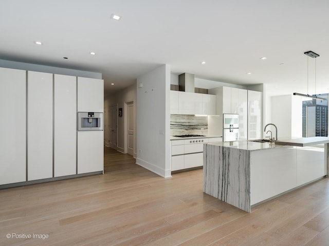 kitchen with backsplash, sink, pendant lighting, white cabinets, and an island with sink