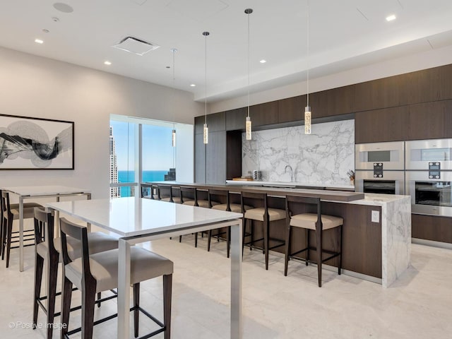 kitchen featuring tasteful backsplash, dark brown cabinetry, a water view, a kitchen island, and hanging light fixtures