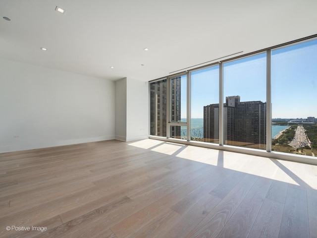 empty room with expansive windows, a water view, and light hardwood / wood-style flooring