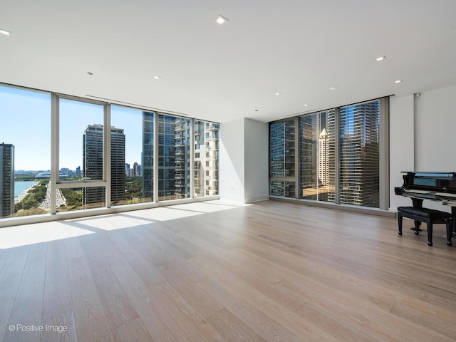 unfurnished living room with floor to ceiling windows, a water view, and light hardwood / wood-style floors