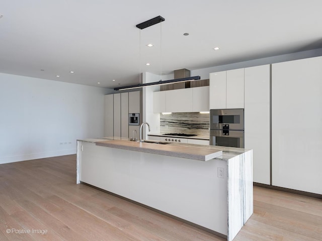 kitchen featuring white cabinetry, sink, tasteful backsplash, an island with sink, and pendant lighting