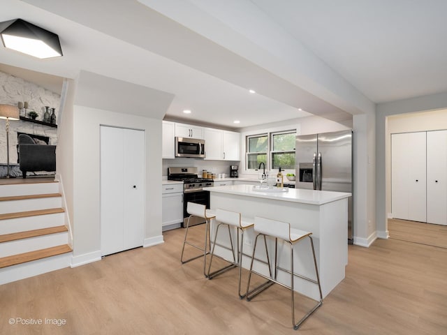 kitchen featuring a center island, white cabinets, a kitchen breakfast bar, light wood-type flooring, and appliances with stainless steel finishes