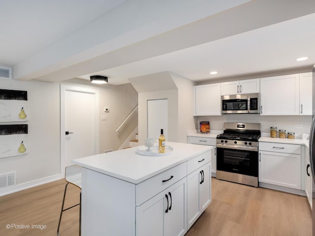 kitchen with light wood-type flooring, a kitchen island, a kitchen bar, white cabinetry, and stainless steel appliances