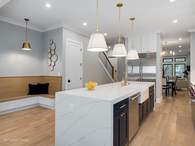 kitchen with a kitchen island with sink, sink, hanging light fixtures, light stone counters, and white cabinetry