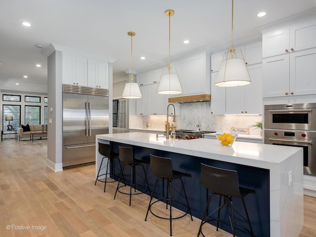 kitchen with a center island with sink, appliances with stainless steel finishes, decorative light fixtures, light hardwood / wood-style floors, and white cabinetry