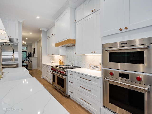 kitchen with white cabinets, stainless steel appliances, light stone countertops, and crown molding