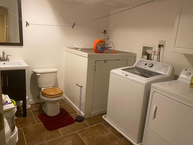 clothes washing area featuring washing machine and dryer, dark tile patterned floors, and sink