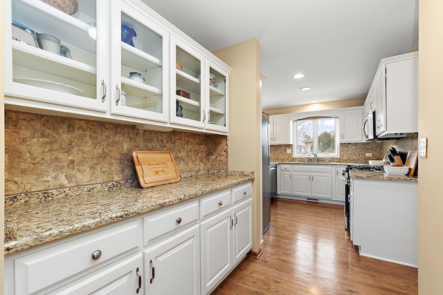 kitchen with white cabinetry, light stone countertops, tasteful backsplash, hardwood / wood-style floors, and stove