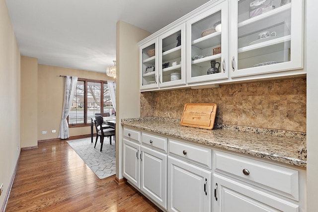 kitchen featuring decorative backsplash, white cabinetry, light stone counters, and light wood-type flooring