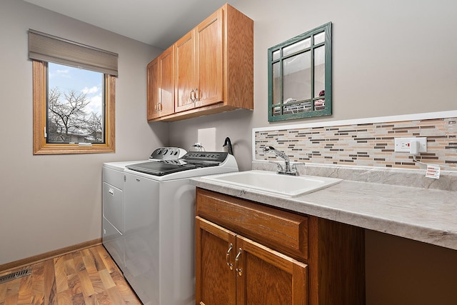 clothes washing area featuring cabinets, light wood-type flooring, washing machine and clothes dryer, and sink