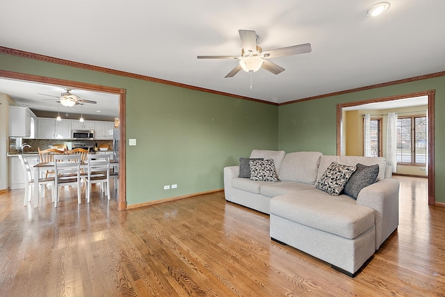 living room with light wood-style floors, ornamental molding, baseboards, and ceiling fan