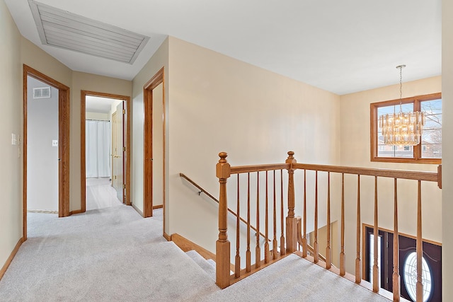 hall with a chandelier, carpet, visible vents, and an upstairs landing