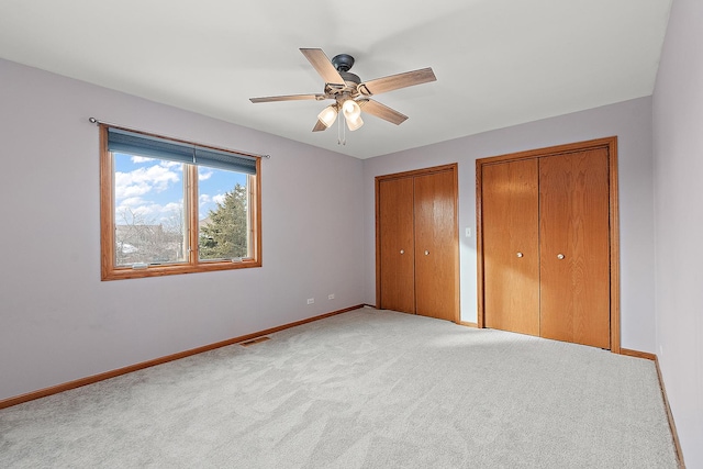 unfurnished bedroom featuring ceiling fan, light carpet, and multiple closets