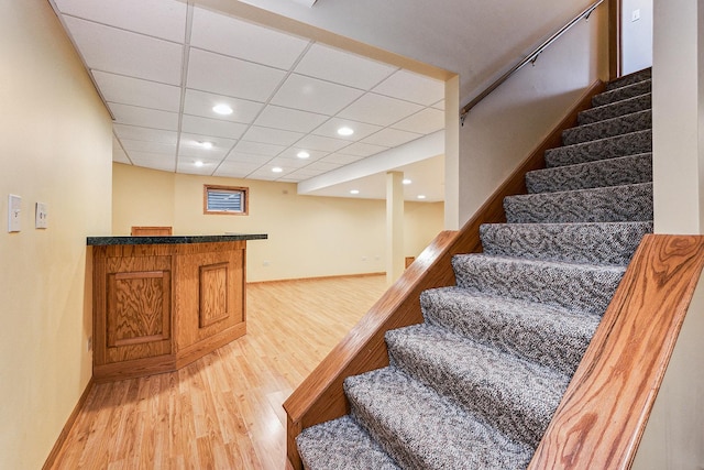 stairs with a dry bar, recessed lighting, wood finished floors, a drop ceiling, and baseboards