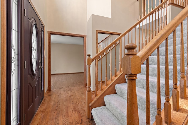 entryway featuring wood finished floors, a towering ceiling, and baseboards