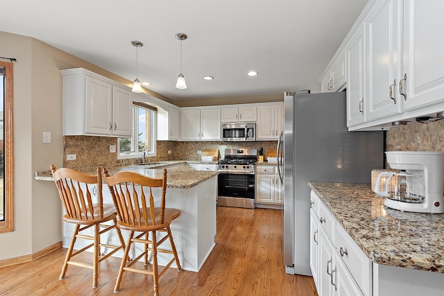 kitchen with appliances with stainless steel finishes, decorative light fixtures, white cabinetry, and a kitchen breakfast bar