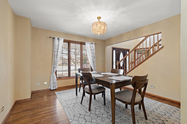 dining area featuring a chandelier, stairs, baseboards, and wood finished floors