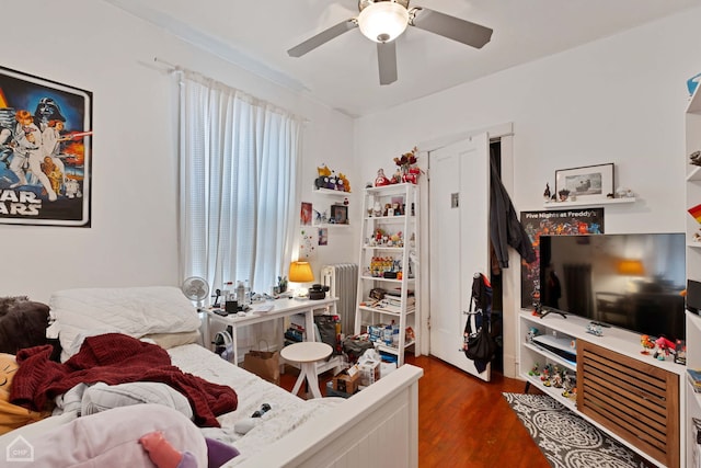 bedroom with ceiling fan, dark wood-type flooring, radiator, and multiple windows