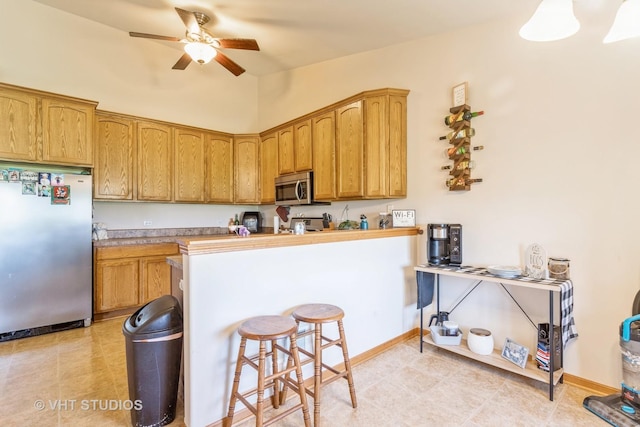 kitchen with light tile patterned floors, stainless steel appliances, ceiling fan, and a breakfast bar area