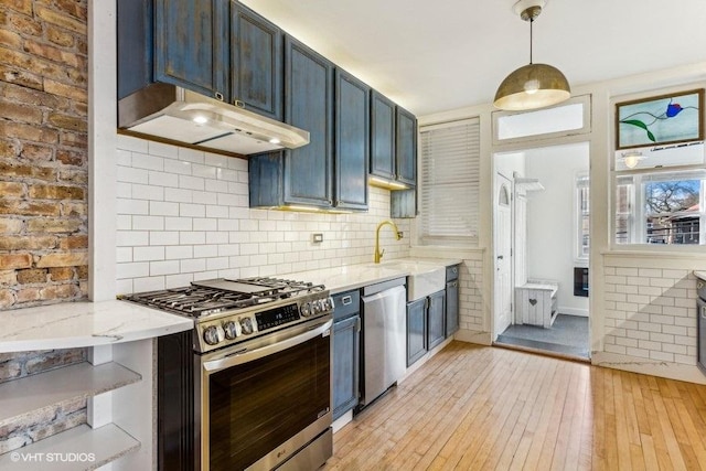 kitchen featuring backsplash, hanging light fixtures, stainless steel appliances, light stone countertops, and light wood-type flooring