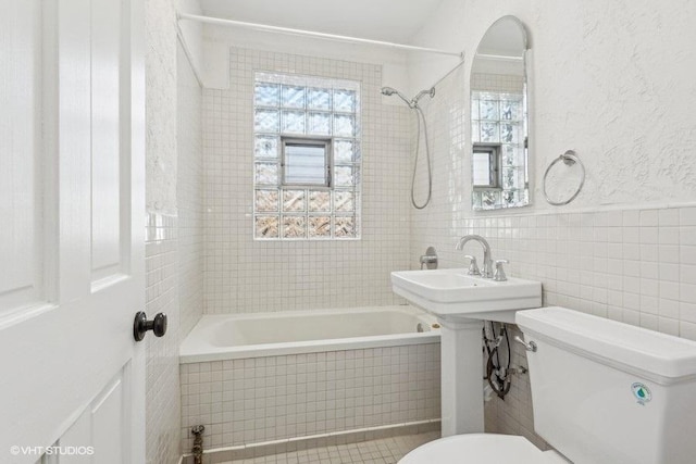 bathroom featuring toilet, tiled shower / bath combo, and tile walls