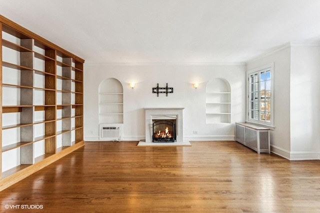 unfurnished living room featuring ornamental molding, a wall unit AC, built in features, and hardwood / wood-style floors