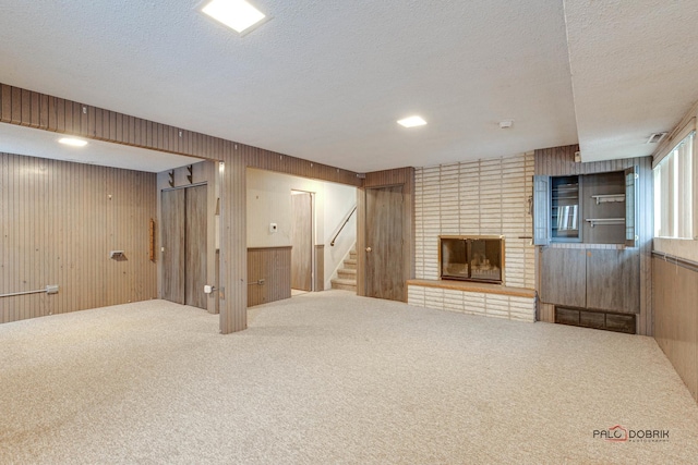 basement with carpet flooring, a textured ceiling, a fireplace, and wood walls