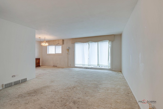 spare room featuring light carpet and a notable chandelier