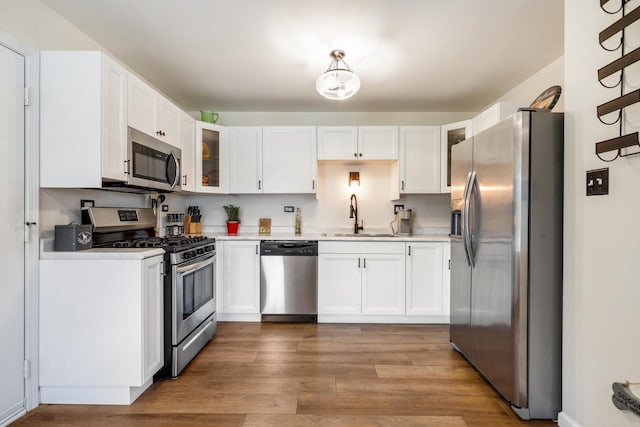 kitchen with light wood-type flooring, white cabinetry, sink, and appliances with stainless steel finishes