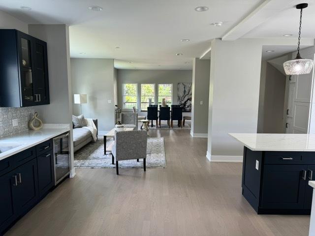 kitchen featuring beverage cooler, light stone counters, backsplash, pendant lighting, and light hardwood / wood-style floors