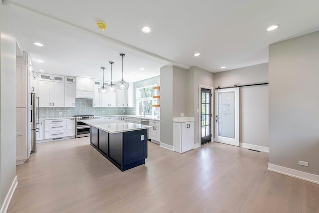 kitchen featuring a kitchen island, a barn door, light hardwood / wood-style flooring, decorative light fixtures, and white cabinets