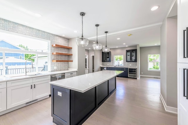 kitchen with a center island, sink, light stone countertops, white cabinetry, and beverage cooler