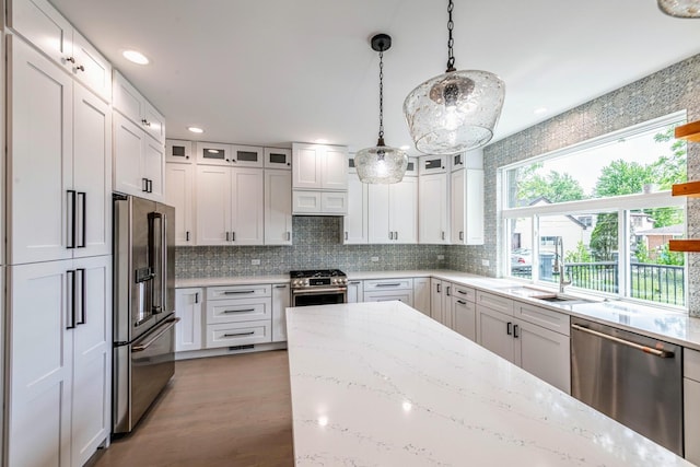 kitchen with high end appliances, light stone counters, decorative light fixtures, dark hardwood / wood-style flooring, and white cabinetry