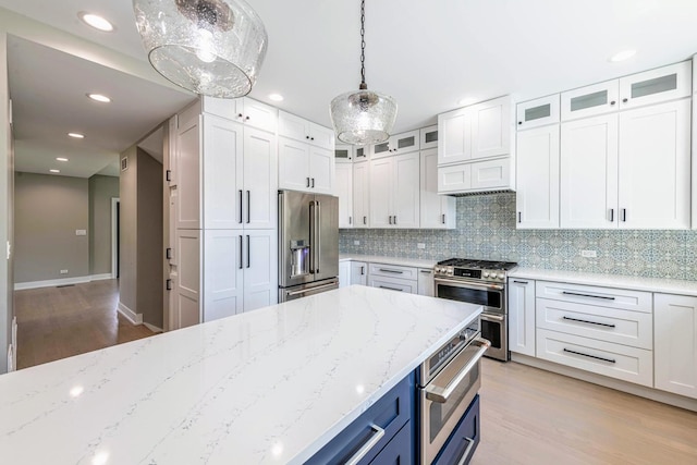 kitchen with light stone counters, decorative light fixtures, high quality appliances, light hardwood / wood-style floors, and white cabinetry