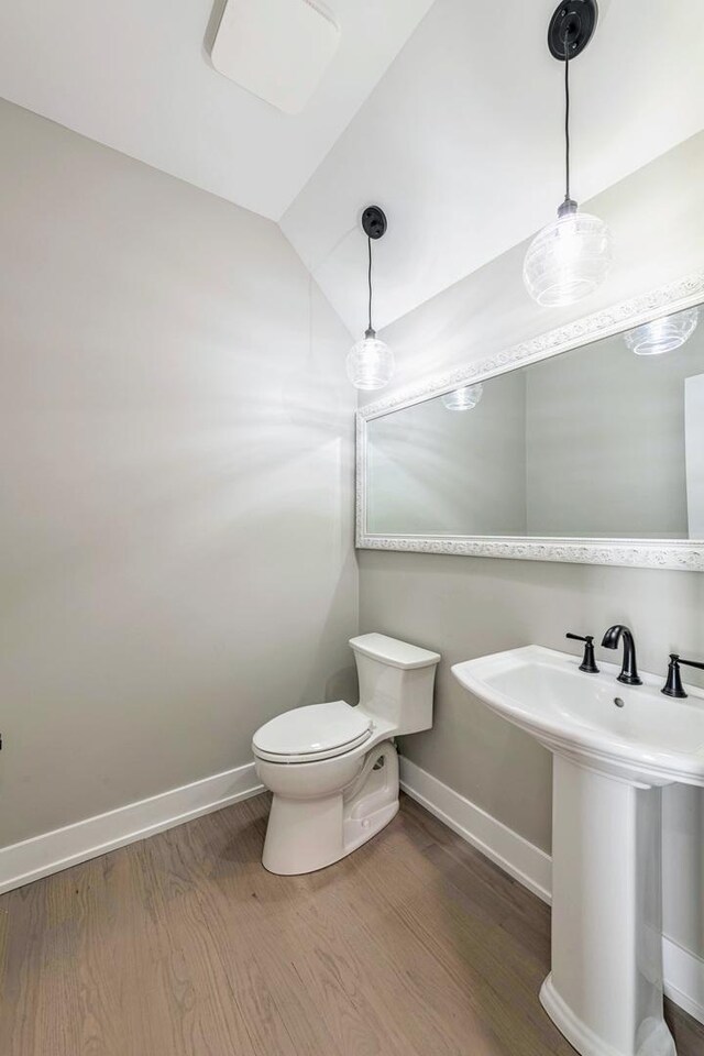 bathroom with hardwood / wood-style floors, toilet, lofted ceiling, and sink