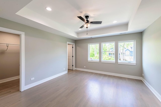 unfurnished bedroom featuring a closet, a raised ceiling, ceiling fan, and light hardwood / wood-style flooring