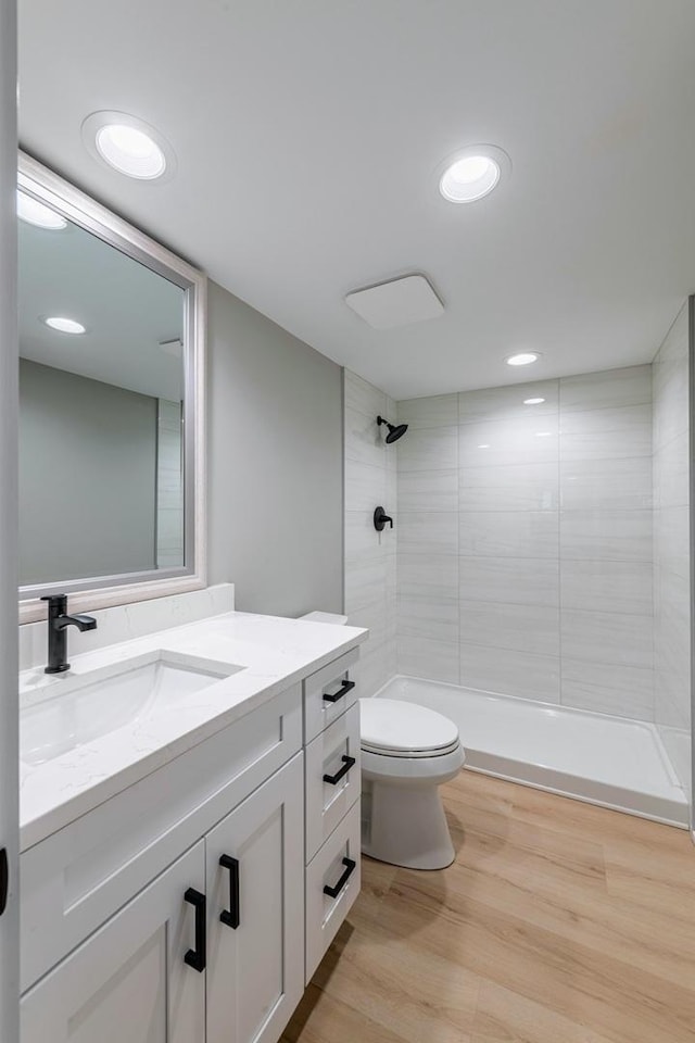 bathroom featuring a tile shower, vanity, wood-type flooring, and toilet