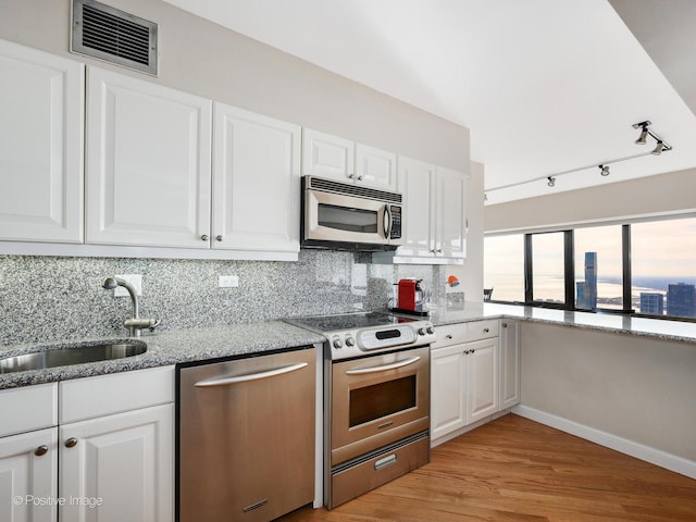 kitchen with appliances with stainless steel finishes, light stone counters, sink, light hardwood / wood-style floors, and white cabinetry