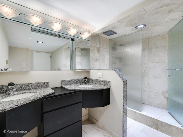 bathroom featuring tile patterned flooring, a tile shower, and vanity