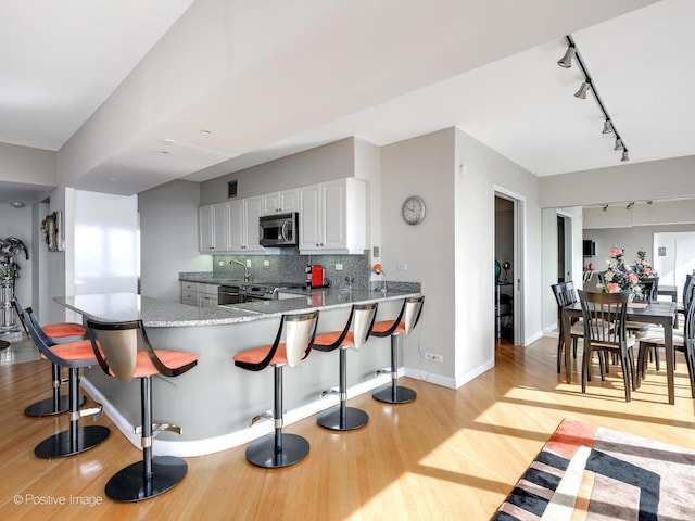 kitchen featuring kitchen peninsula, a kitchen breakfast bar, backsplash, stainless steel appliances, and white cabinets