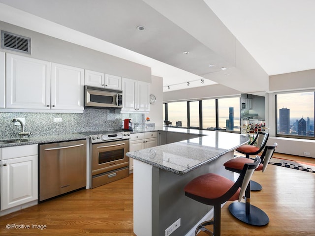 kitchen with white cabinets, decorative backsplash, light stone countertops, appliances with stainless steel finishes, and a breakfast bar area