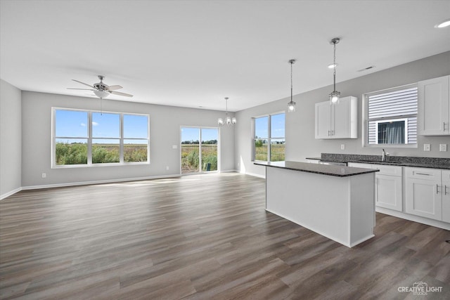 kitchen featuring dark hardwood / wood-style flooring, ceiling fan with notable chandelier, white cabinets, a kitchen island, and hanging light fixtures